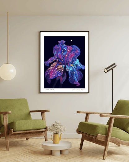 Framed artwork of a rainbow colorful flower that looks galactic like space on a black background with white boarders on a beige wall in a modern living room with green chairs and a small table. 