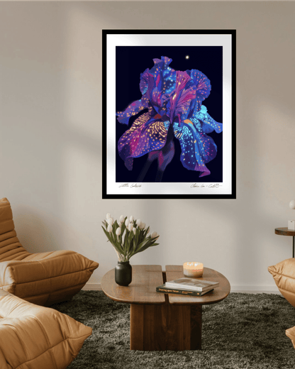 Framed artwork of a rainbow colorful flower that looks galactic like space on a black background with white boarders on a beige wall in a trendy living room with hipster chairs and vase of white tulips on a coffee table. 