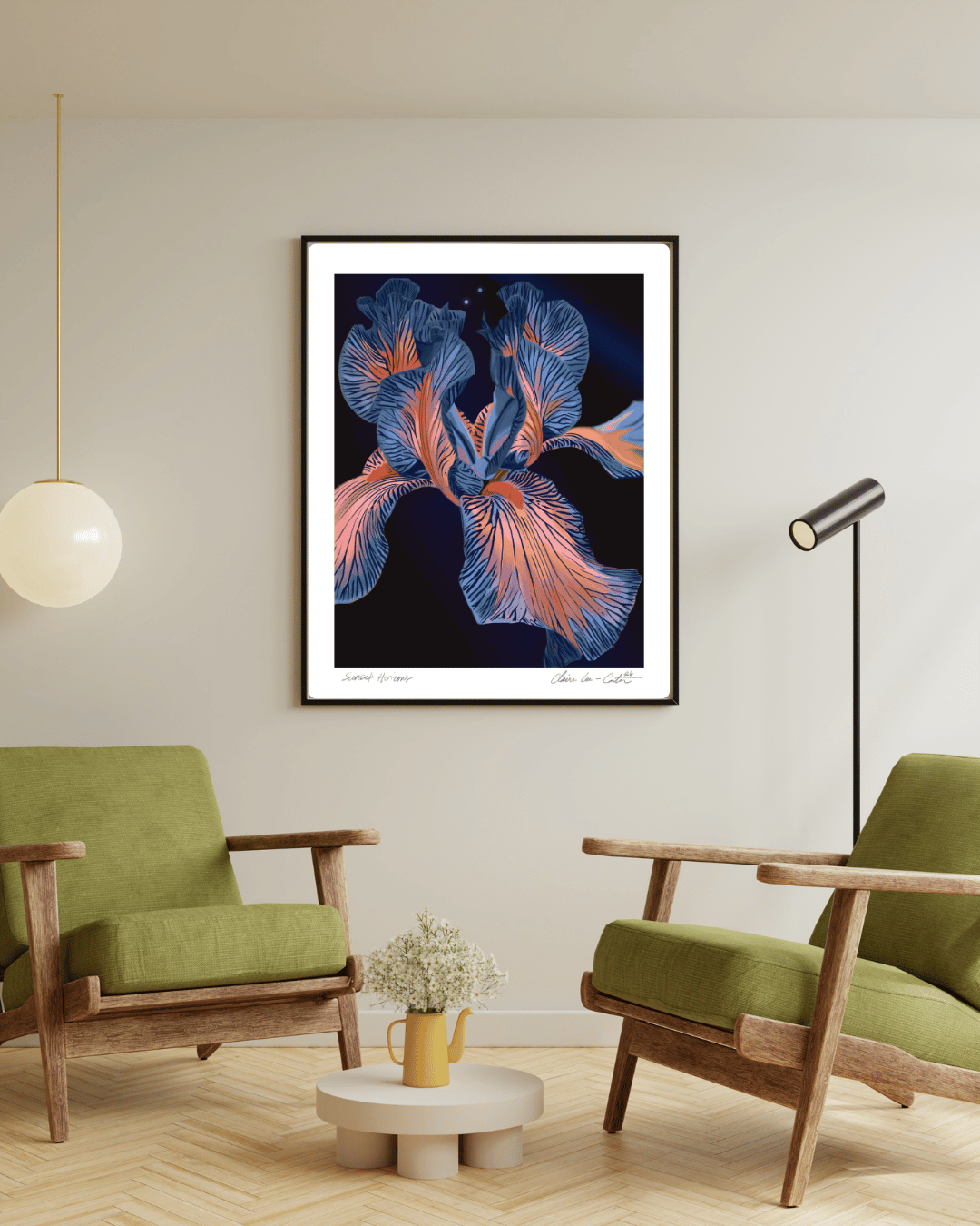 Framed fine art print of a blue and pink iris flower with a black background and a white boarder on a beige wall  in a modern living room with green chairs and a small table. 